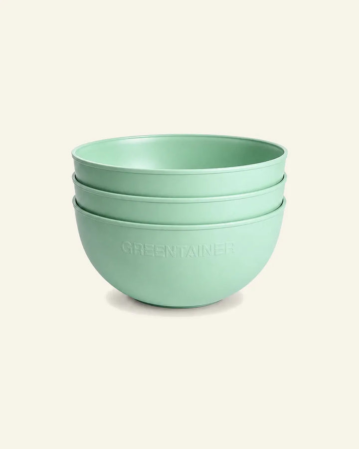 Three stacked mint green bowls with the brand name 'GREEN TAINER' embossed on the front, set against a solid cream background.