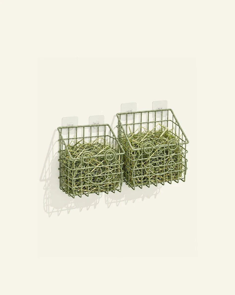 Two sage green wire hay feeders filled with hay, mounted on adhesive wall hooks